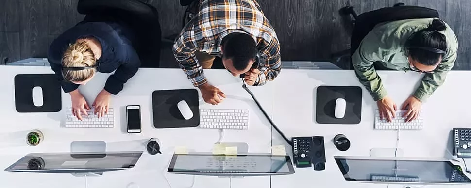 Three people working at computers in an office setting, viewed from above.