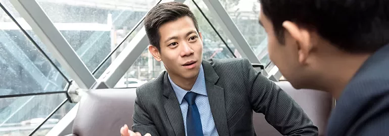 Two colleagues in suits having a discussion in a modern office setting.