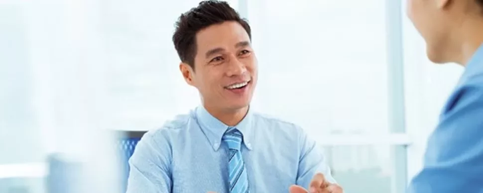 Smiling man in a blue shirt talking with a colleague in an office.