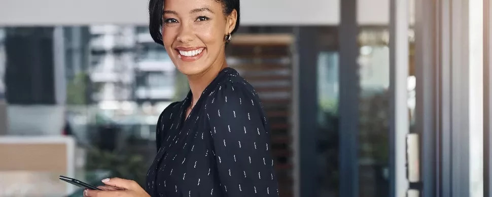 Smiling woman in a black blouse holding a smartphone indoors.