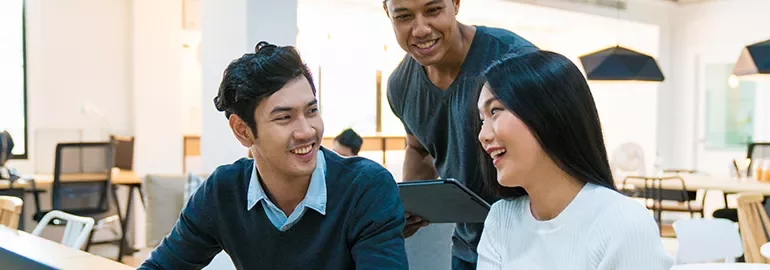 Three colleagues laughing and working together in a modern office.