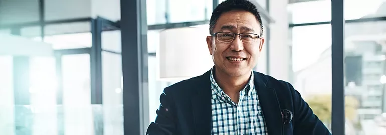 Smiling person in a checked shirt and blazer, in a bright modern office.