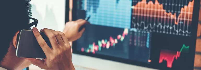 Person analyzing financial charts on a computer screen, talking on the phone.