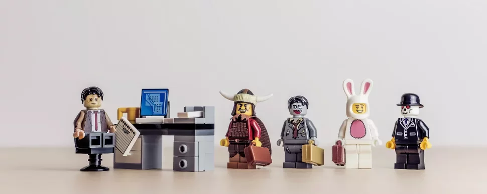 Lego figures dressed in various costumes standing in line at an office desk.