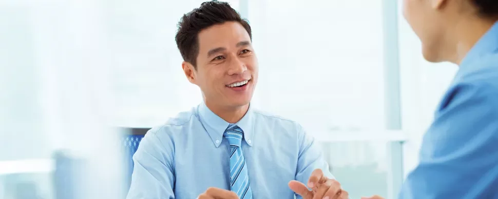 Man in blue shirt smiling at a colleague during a meeting.