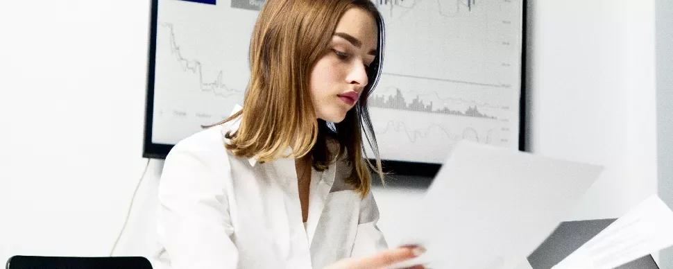 Woman in white shirt reviewing documents in front of graph.