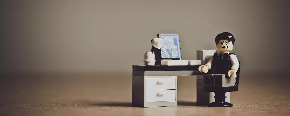 Lego figure at a desk with a computer, looking distressed.