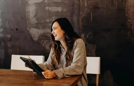 Woman smiling while holding a tablet at a wooden table