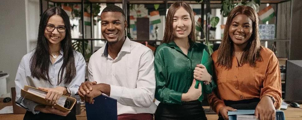 Four colleagues smiling and holding folders in an office setting.