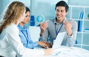 Three colleagues having a discussion at a table with a laptop.