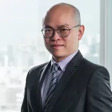 Man in a suit and tie standing in front of a window with a cityscape background.