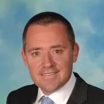 Portrait of a smiling man in a suit with a blue sky background.
