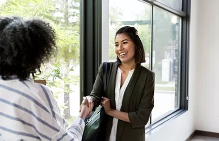 Two women shaking hands by a sunlit window.