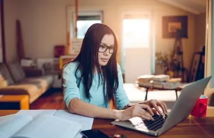 Woman with glasses working on a laptop in a cozy living room.